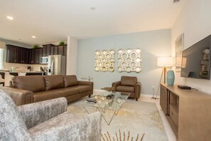 A modern living room with a sofa, armchair, and coffee table, a kitchen in the background, and decorative wall art. - Solara Resort - 25995 (Kissimmee)
