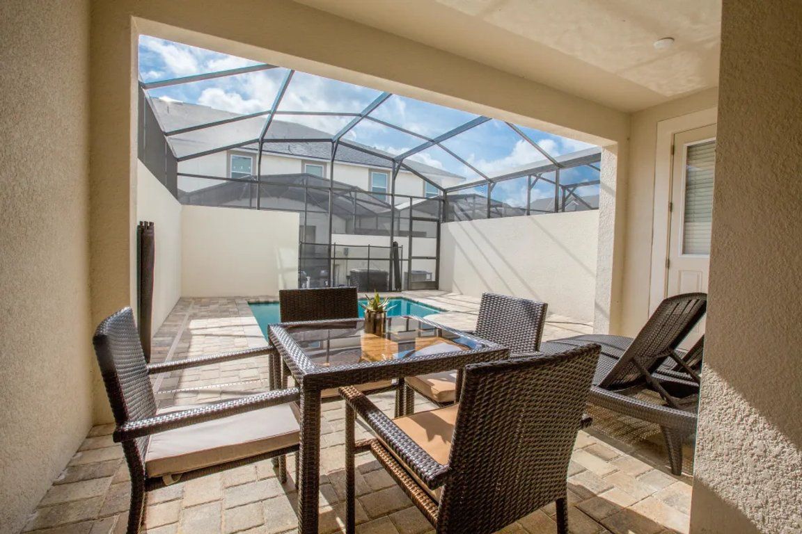 A glass-enclosed patio with a table and chairs, a pool, and a view of a house.