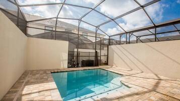 A swimming pool with a glass ceiling structure, surrounded by walls and a brick floor.