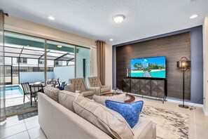 A modern living room with a sofa, chairs, a TV, and a pool view. - Windsor at Westside - 26139 (Kissimmee)