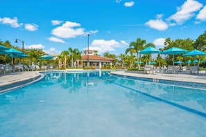 A swimming pool with lounge chairs and umbrellas, surrounded by palm trees and a building in the background. - Vista Cay - 26552 (Orlando)