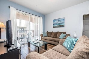 A living room with a sofa, a glass coffee table, a television, and a painting on the wall. - Vista Cay - 26552 (Orlando)