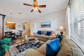 A living room with a sofa, coffee table, and a dining area with chairs and a table. - Vista Cay - 27374 (Orlando)