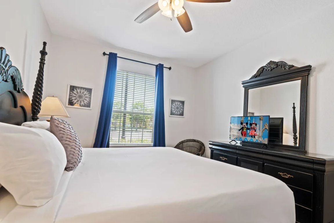 A hotel room with a bed, a ceiling fan, a dresser, a mirror, and a window with curtains.