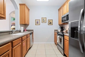A kitchen with wooden cabinets, a stainless steel refrigerator, a microwave, and a dishwasher. There are three framed pictures on the wall. - Vista Cay - 27374 (Orlando)