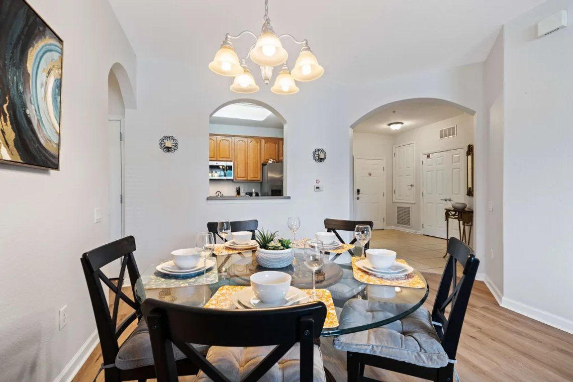 A dining area with a round glass table, black chairs, and a chandelier.