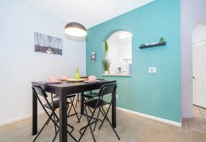 Un comedor con una mesa y sillas negras, una lámpara colgante y paredes color turquesa.