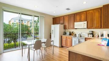 Una cocina moderna con armarios de madera, un refrigerador, un microondas y un comedor con mesa y sillas.