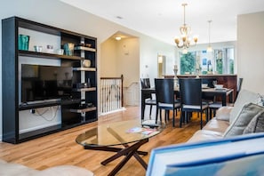 A modern living room with a glass coffee table, a sofa, and a dining area with chairs and a chandelier. - Vista Cay - 28754 (Orlando)