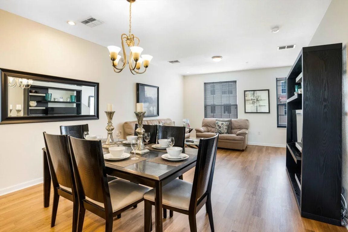 Un comedor con una mesa y sillas de madera, un candelabro y un espejo grande en la pared.