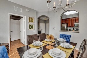 A dining area with a table set for six, a chandelier, and a kitchen visible through an archway. - Vista Cay - 28755 (Orlando)