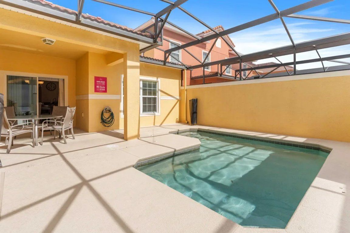 An indoor swimming pool with a glass ceiling, a seating area with chairs, and a view of the outside buildings.