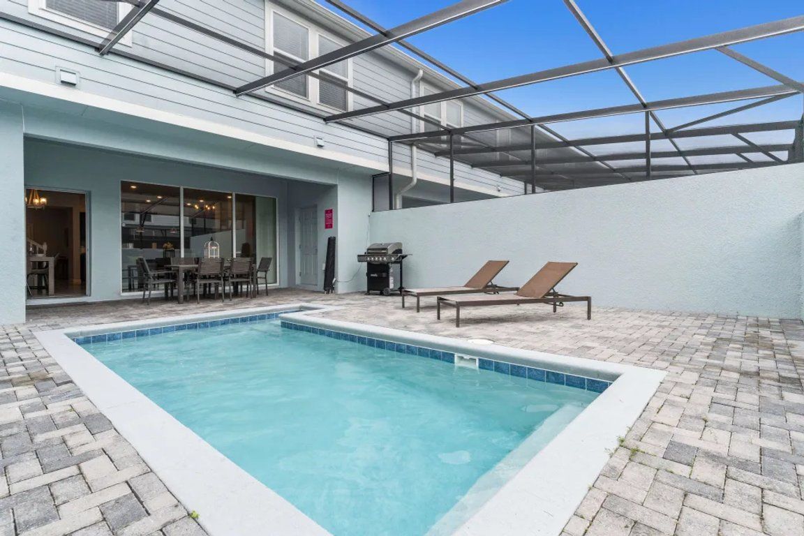 Una piscina con sillones de descanso, una parrilla y un patio cubierto.