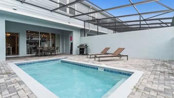 Una piscina con sillones de descanso, una parrilla y un patio cubierto.