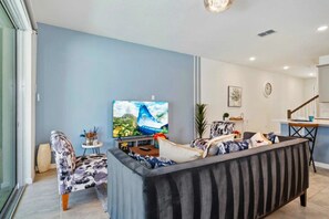 Ein Wohnzimmer mit einer Couch, einem Fernseher und einem Essbereich mit Stuhl und Tisch.