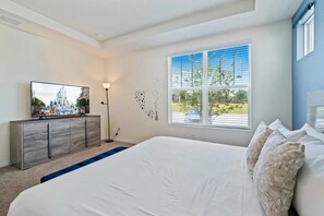 Ein Schlafzimmer mit einem großen Bett, einem Schminktisch, einem Fernseher und einem Fenster mit Jalousien.