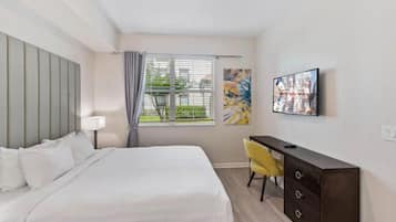 A hotel room with a bed, a desk, a chair, a TV, and a window with curtains.