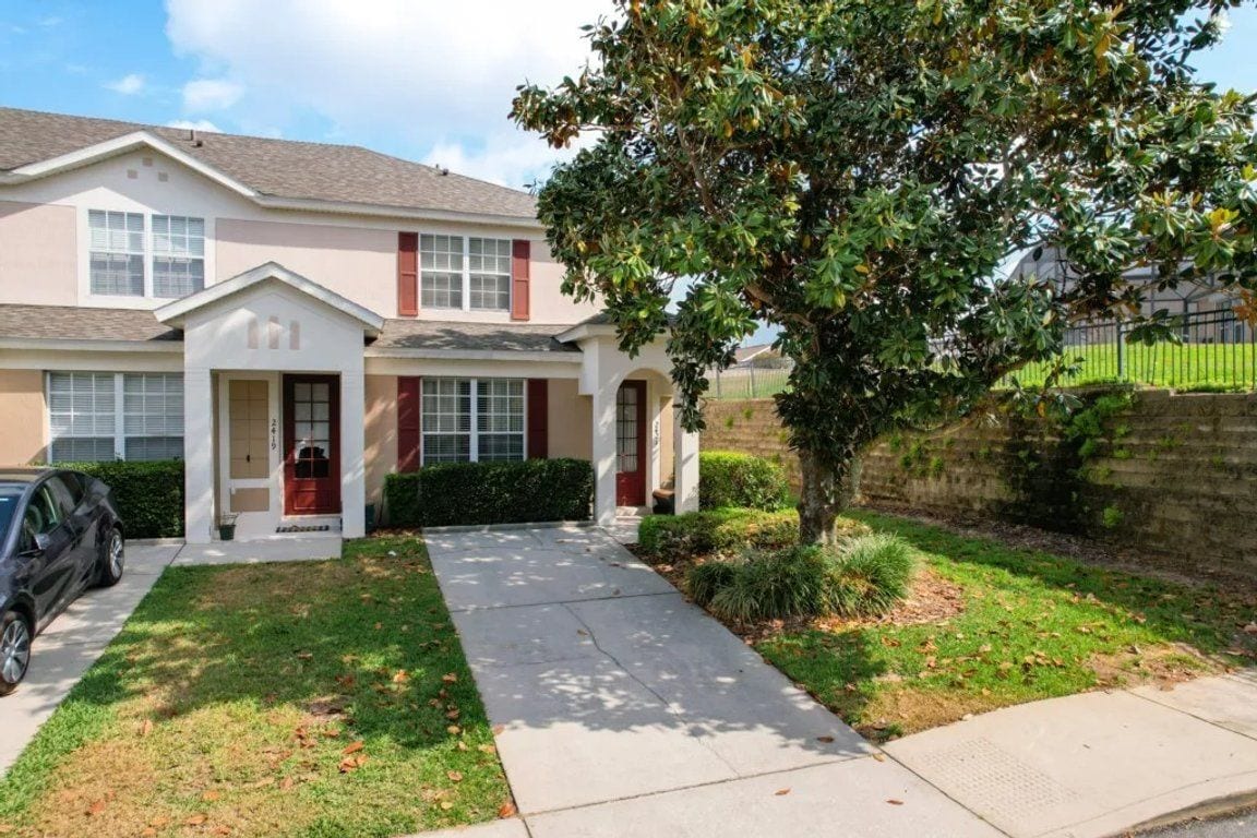 A two-story residential house with a front entrance, a driveway, and a tree in the yard.