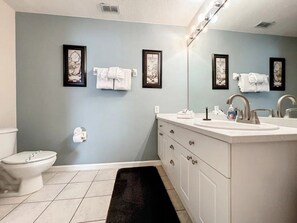 Un bagno con il water, un lavandino con uno specchio e opere d'arte incorniciate appese al muro.