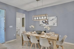 A dining area with a wooden table, grey chairs, a chandelier, and artwork on the wall. - Solara Resort - 29566 (Kissimmee)