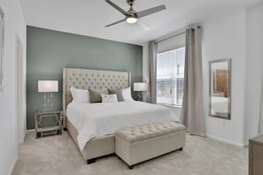 A bedroom with a tufted headboard, a bed with white linens, a bedside table with lamps, a window with blinds, and a ceiling fan. - Solara Resort - 29566 (Kissimmee)