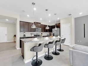 A modern kitchen with a central island, bar stools, and pendant lighting. - Windsor Island - 33034 (Davenport)