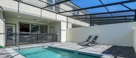 A swimming pool with a glass ceiling, a covered patio area, and a view of a white building.