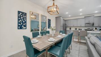A modern kitchen with grey cabinets, a dining area with teal chairs, and a large mirror above the table.