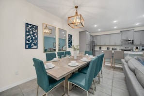 Une cuisine moderne avec des meubles gris, un coin repas avec des chaises turquoise et un grand miroir au-dessus de la table.