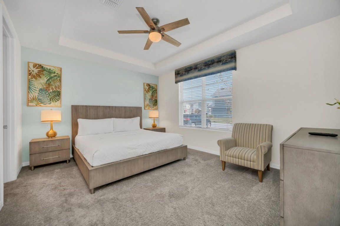 A bedroom with a bed, nightstands, a chair, a desk, a ceiling fan, and artwork on the walls.