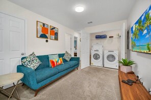 A living room with a blue sofa, a small round table, and a washing machine in the background. - Solara Resort - 34692 (Kissimmee)