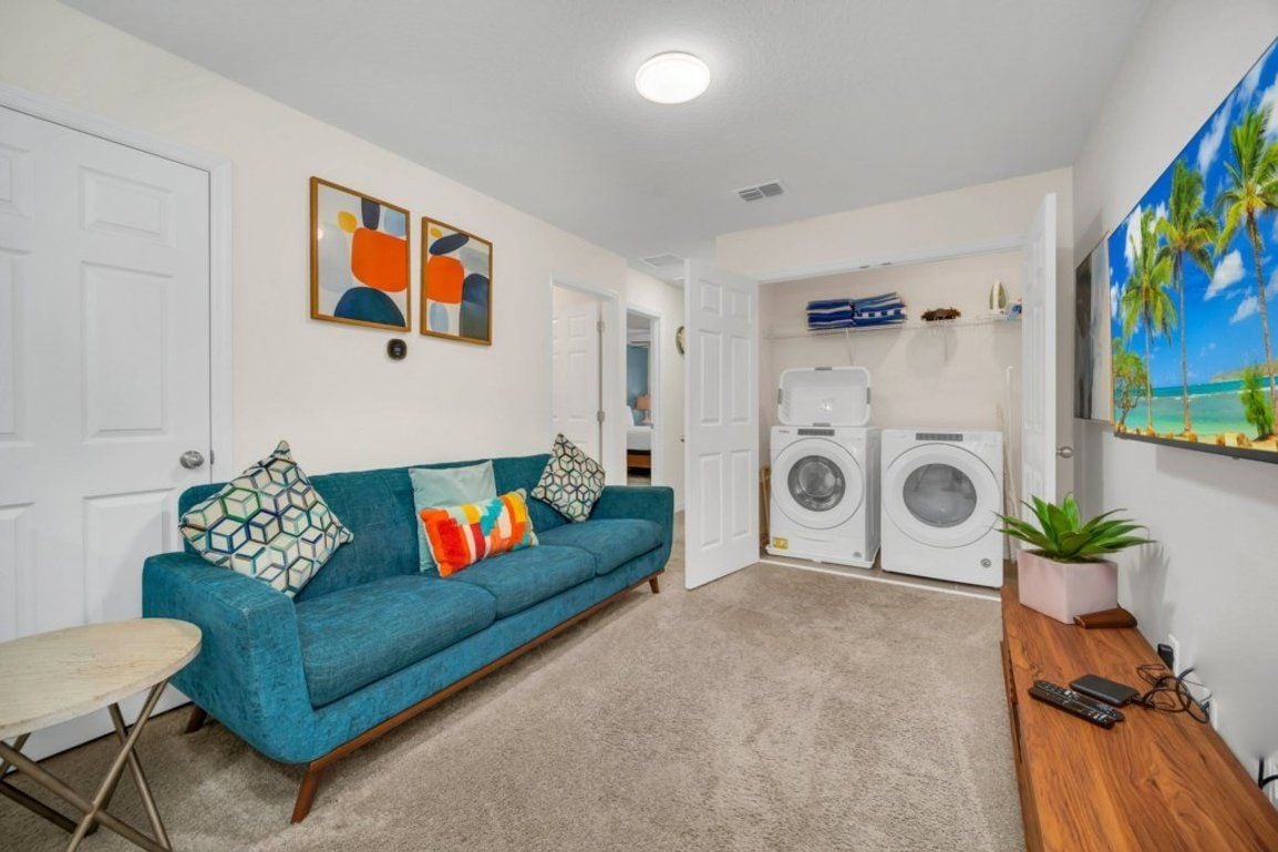 A living room with a blue sofa, a small round table, and a washing machine in the background.