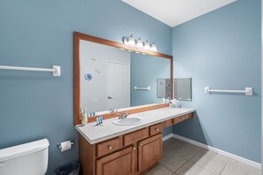 A bathroom with a white toilet, a sink with a mirror above it, wooden cabinets, and a towel rack. - Windsor Palms - 34815 (Kissimmee)