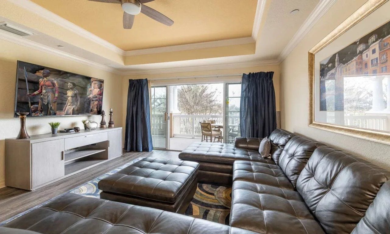 Un salon spacieux avec un grand canapé en cuir, un téléviseur à écran plat et un ventilateur de plafond.