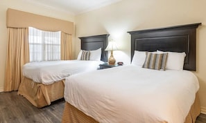Habitación de hotel con dos camas, una mesita de noche con lámpara y un ventanal con cortinas.