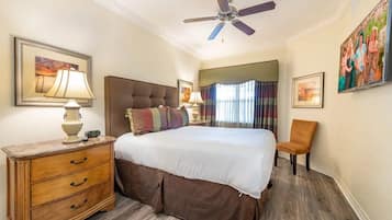 Une chambre d’hôtel avec un lit, une table de chevet, une chaise, un ventilateur de plafond et des œuvres d’art accrochées aux murs.