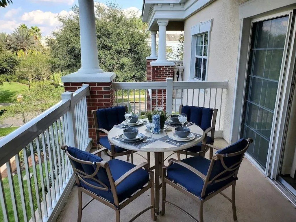 Een balkon met een ronde tafel voor vier personen, omringd door stoelen met blauwe kussens.