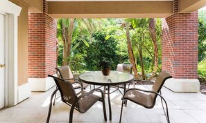 Eine Terrasse im Freien mit einem runden Tisch und Stühlen, umgeben von Backsteinmauern und üppigem Grün.