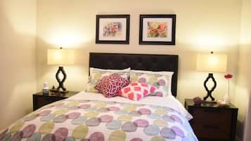 A bedroom with a bed, two nightstands, two wall-mounted lamps, and two framed floral paintings.