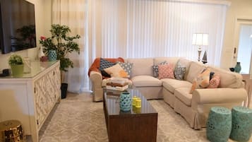 Sala de estar com sofá bege, mesa de centro de vidro e almofadas decorativas.