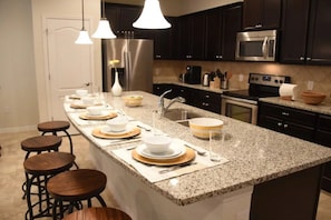 Cozinha moderna com bancadas de granito, eletrodomésticos de aço inoxidável e banquetas.