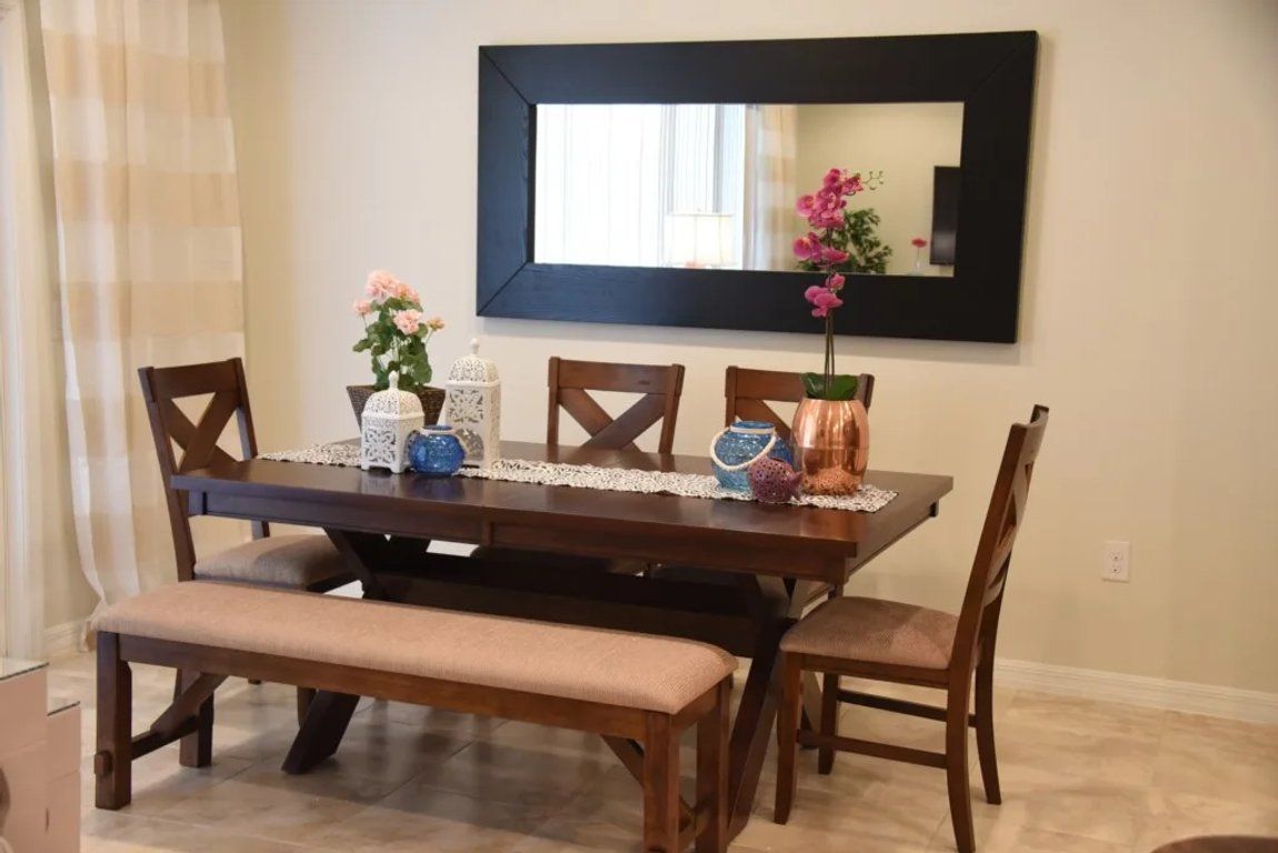 A dining area with a dark wooden table, four chairs, a bench, and a large mirror on the wall.