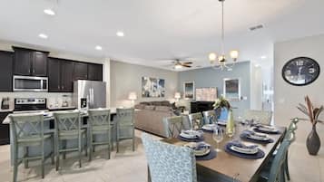 A modern kitchen with dark cabinets, a microwave, and a refrigerator. There is a dining area with a table set for four, chairs, and a chandelier.