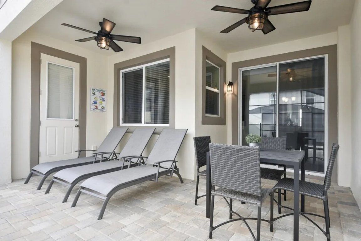 A sunroom with a ceiling fan, a table with chairs, and a window with blinds.