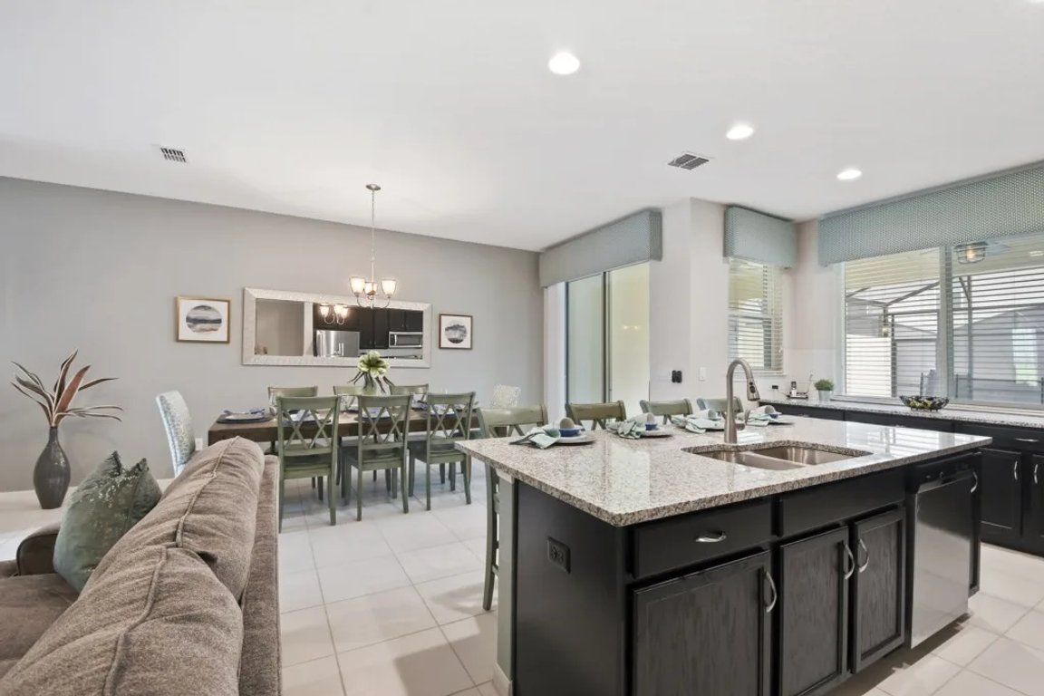 A modern kitchen with a central island, dining area, and a living space with a sofa.