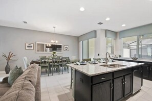 A modern kitchen with a central island, dining area, and a living space with a sofa. - Solara Resort - 2841 (Kissimmee)
