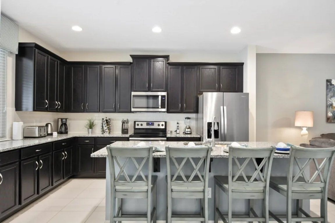 A modern kitchen with dark cabinets, stainless appliances, and a central island with bar stools.