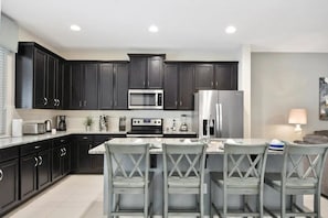 A modern kitchen with dark cabinets, stainless appliances, and a central island with bar stools. - Solara Resort - 2841 (Kissimmee)