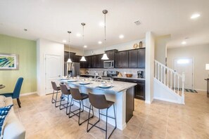A modern kitchen with a central island, bar stools, and pendant lighting. - Windsor at Westside - 4763 (Kissimmee)