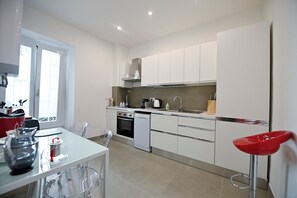 A modern kitchen with white cabinetry, a dining area with a table and chairs, and a red bar stool. - Three steps from Spanish Steps, Via Veneto, and Villa Borghese (ROMA - RM)